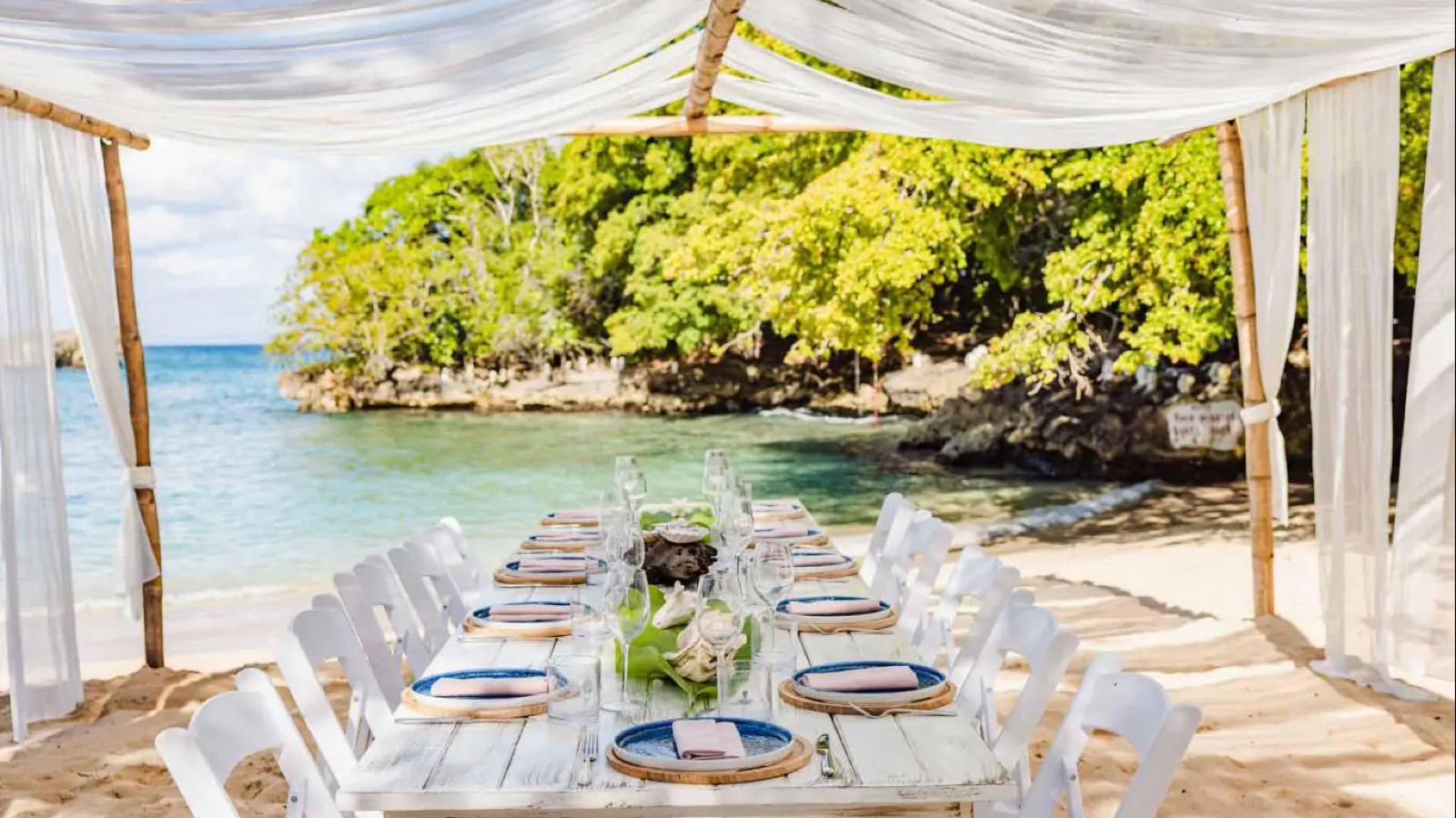 Table laid on the sand beneath white drapes