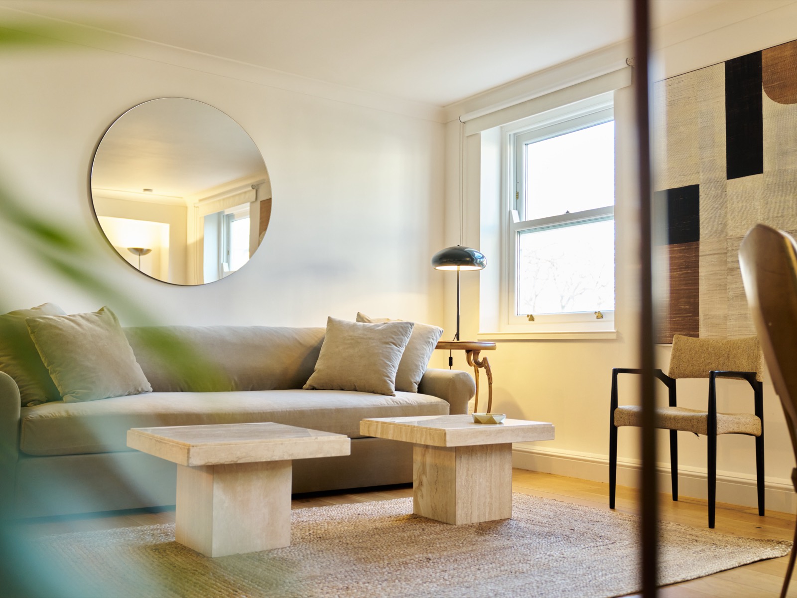 Sofa and travertine tables beneath a round mirror