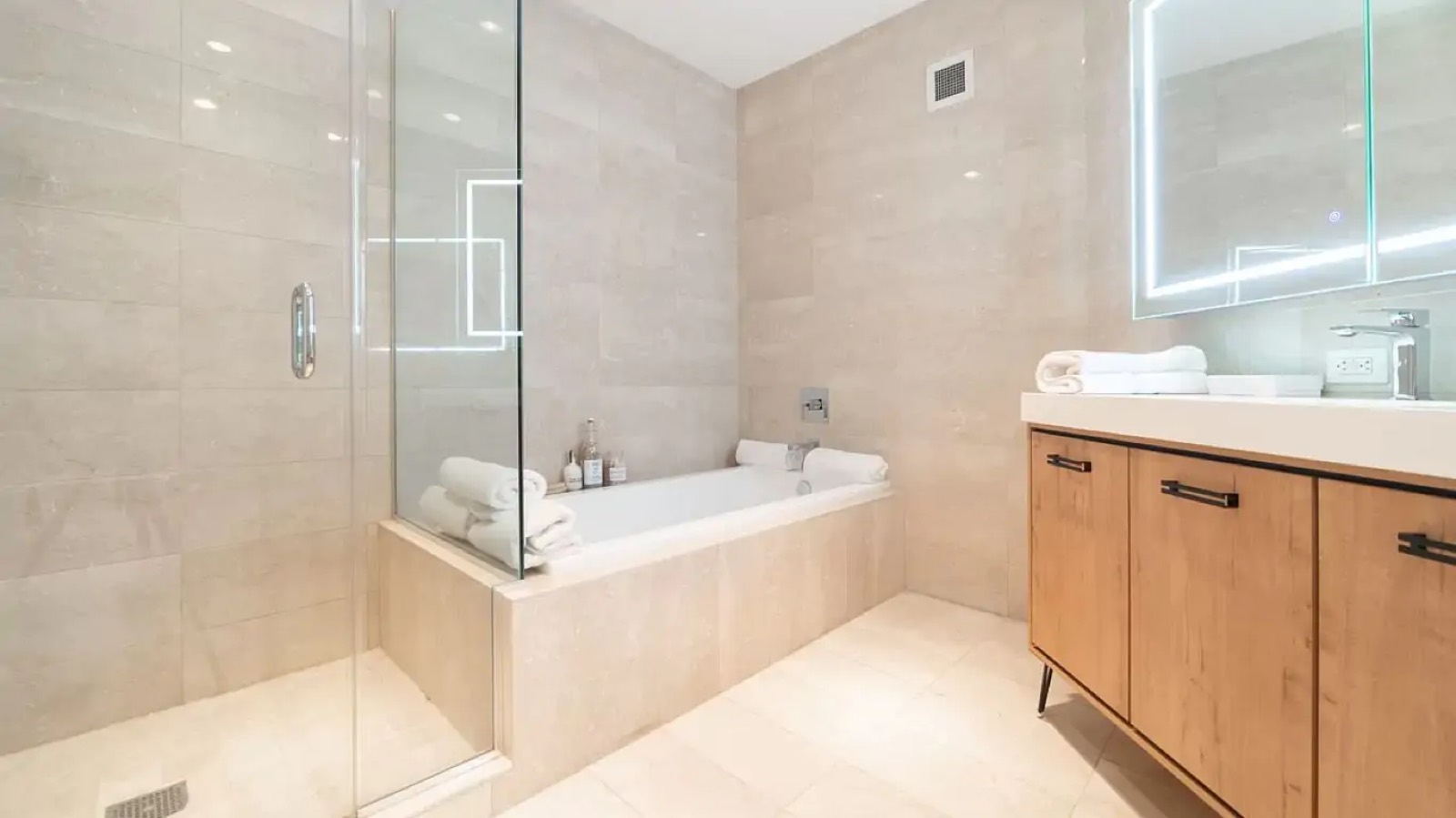 Stone bathroom with bath, shower and lit mirror