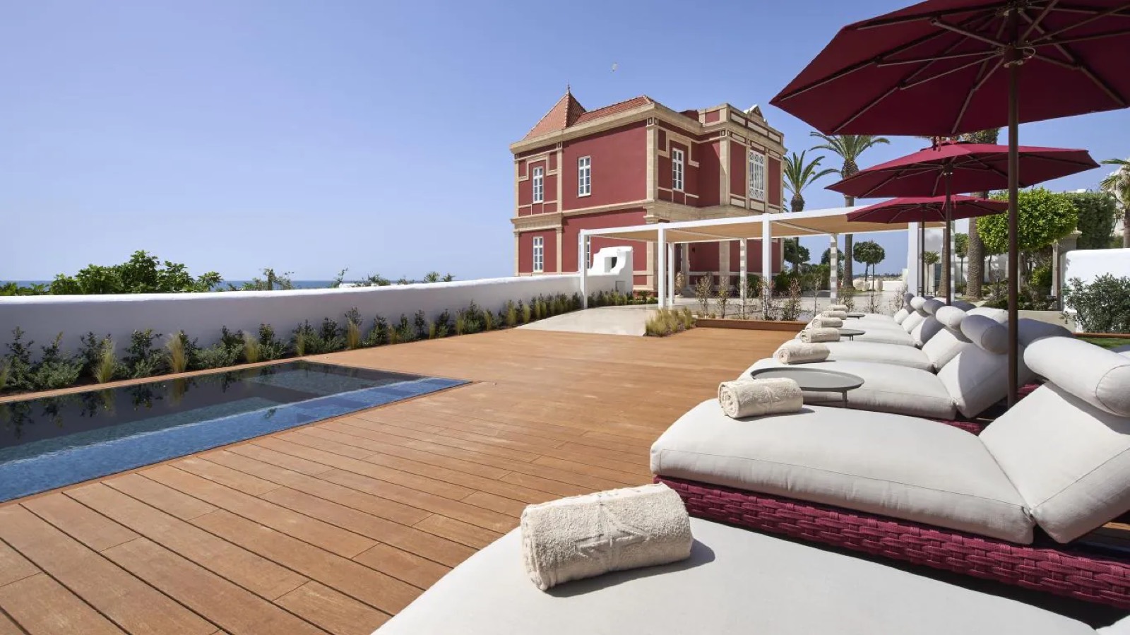 Pool and sun loungers under red parasols